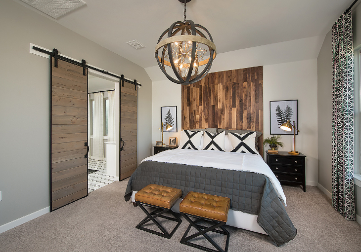A beautiful bedroom features a shiplap headboard, modern chandelier and barn doors that lead to the bathroom.