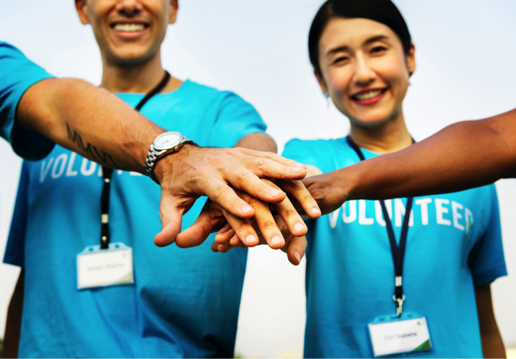 four people wearing turquoise t-shirts volunteering putting their hands together in team spirit