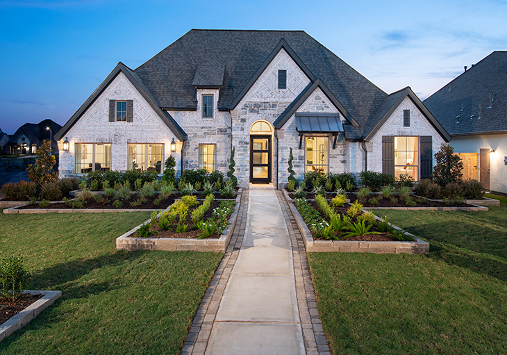 Sidewalk leads to large white Perry Home in Texas with dark grey accents and well-kept lawn and landscaping.