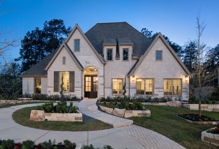 A beautiful stone-walled two-story home sits among a lush, green lawn and spiral-cut trees.