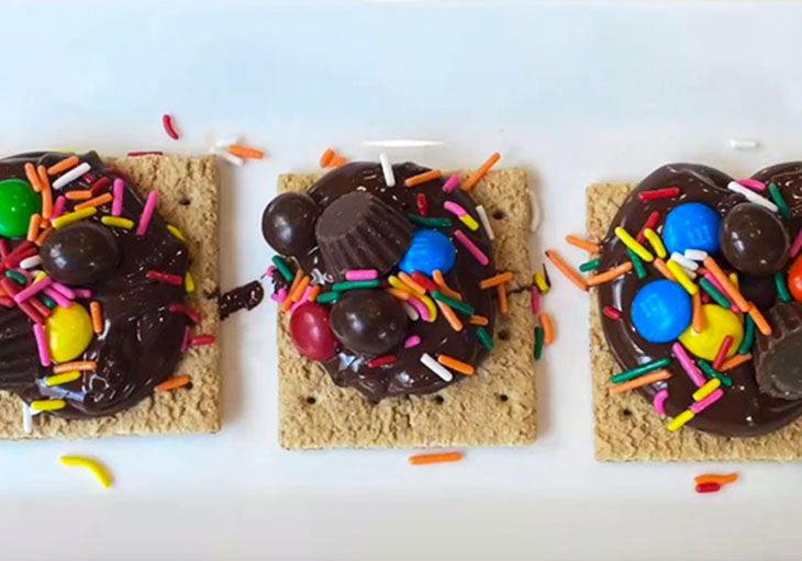 White square dishes contain graham crackers topped with chocolate, sprinkles, marshmallows and other candies.