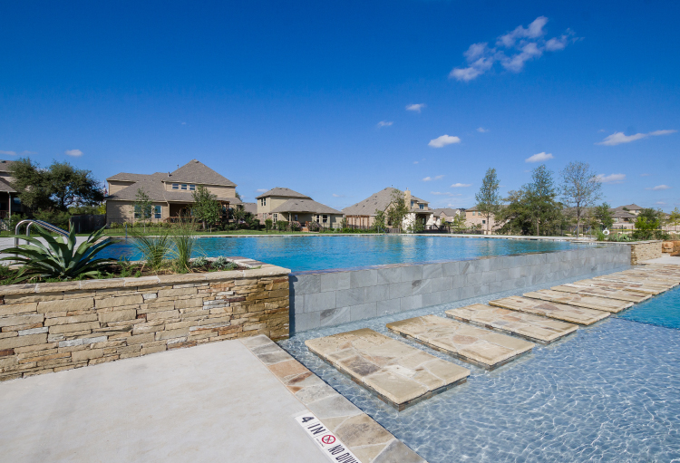 A resort-style pool with tan stepping stones surrounded by new construction homes.
