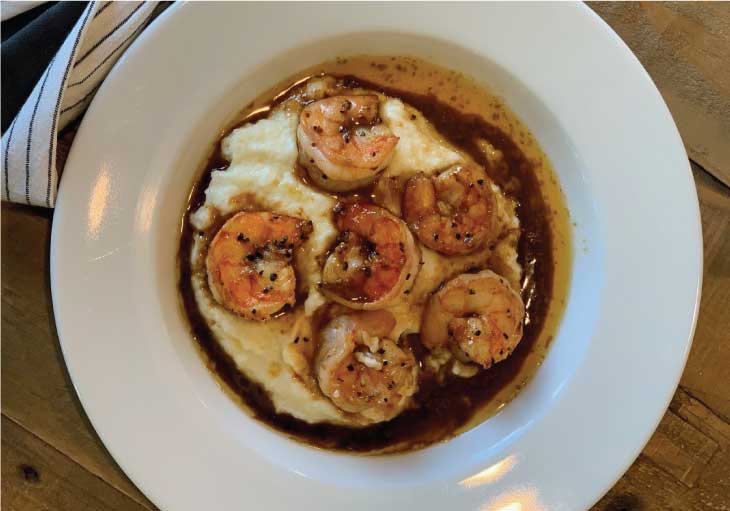 Cheesy grits topped with flavorful shrimp sits in a white bowl.