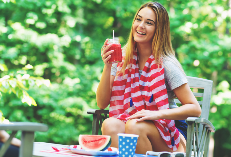 A girl dressed in a red, white and blue shawl sips a refreshing frozen drink while laughing with friends.